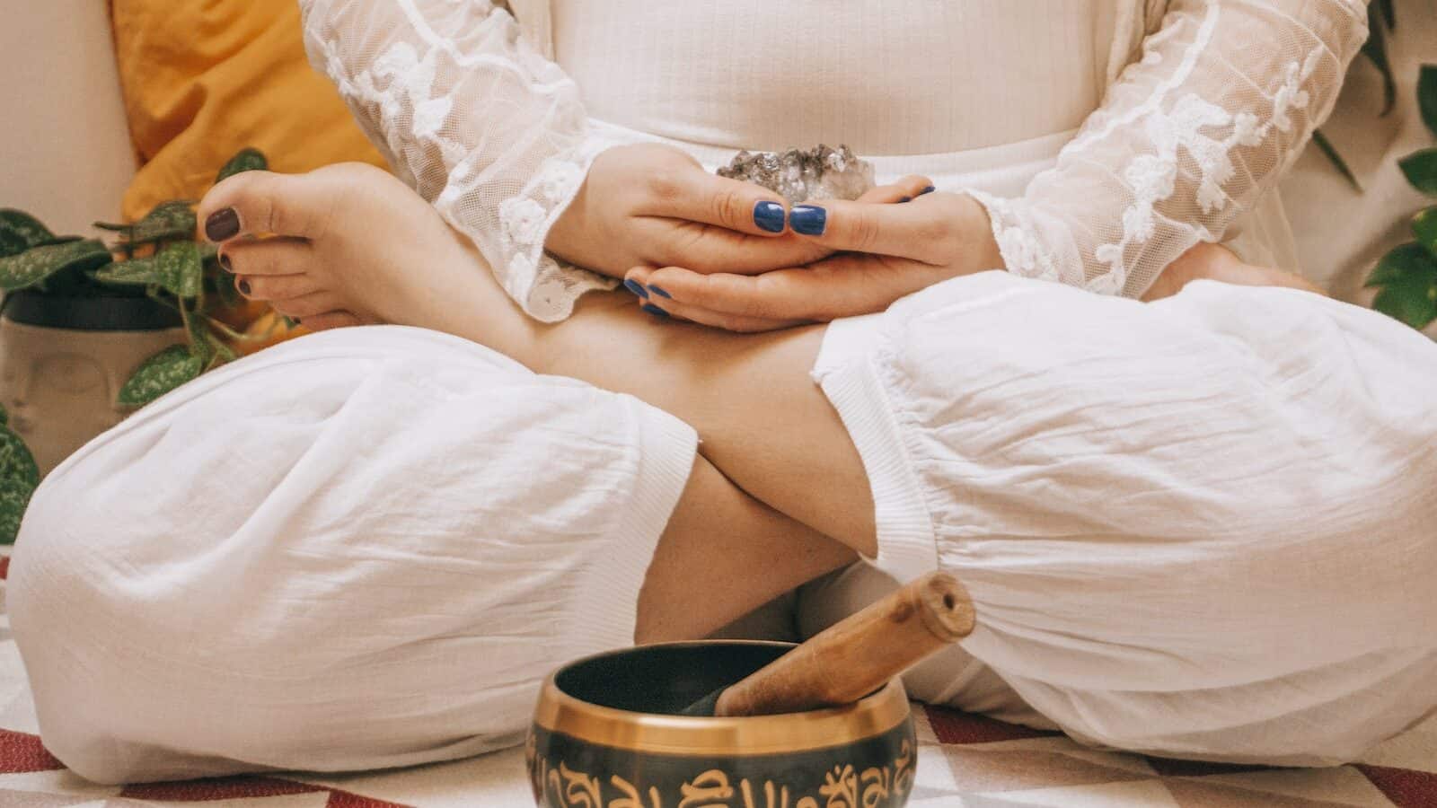 A Woman in Lotus Position Holding a Crystal Sitting Near a Metal Bowl