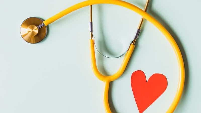 Medical stethoscope with red paper heart on white surface