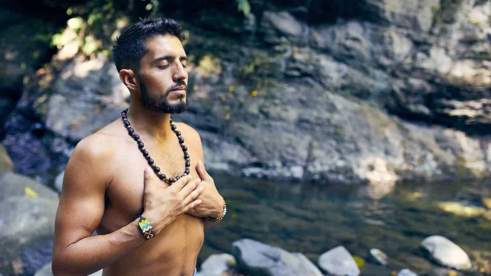 topless man wearing black beaded necklace and blue denim shorts standing on rocky shore during daytime