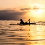 silhouette of woman lying on surfboard at the sea