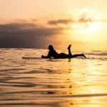 silhouette of woman lying on surfboard at the sea