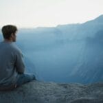 man in gray shirt sits on cliff