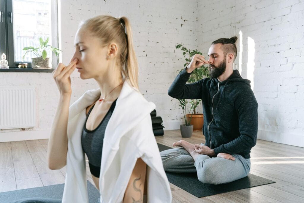 A man and woman practicing mindful yoga and breathing exercises in a serene indoor setting.