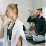 A man and woman practicing mindful yoga and breathing exercises in a serene indoor setting.