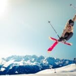 person in brown jacket doing snow ski blade trick