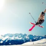 person in brown jacket doing snow ski blade trick