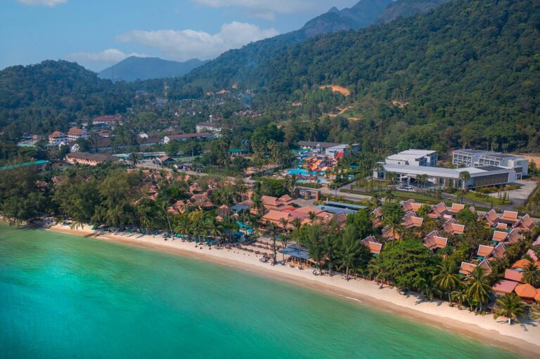 Aerial view of beachfront resort and lush mountains.