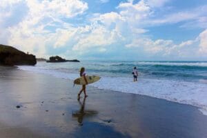 Two surfers walking along sandy beach shoreline