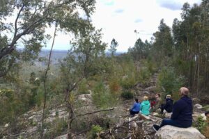 People sitting on hillside overlooking forested valley