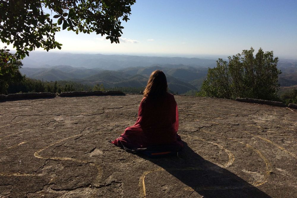 Person sitting on cliff overlooking mountain landscape