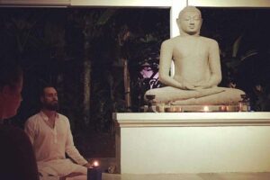 Man meditating before large Buddha statue indoors