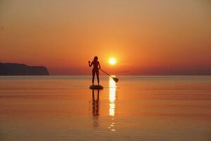 Silhouette paddleboarder at sunset on calm sea