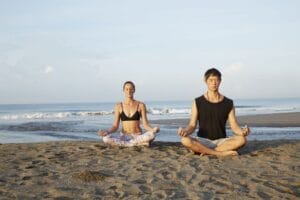 Two people meditating on a sandy beach