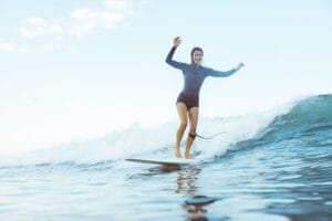 Woman surfing on ocean wave under bright sky