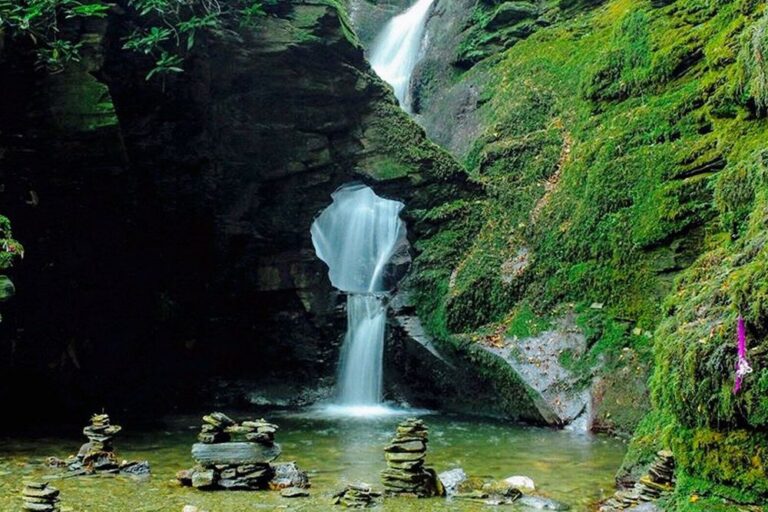 Waterfall flowing through rock arch into mossy pool