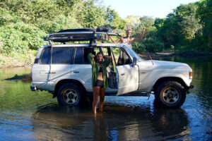 SUV parked in shallow river with two travelers