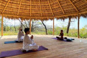Three people meditating in open-air thatched pavilion