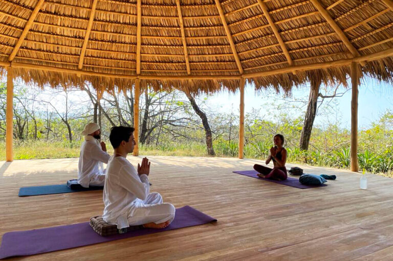 People meditating in open-air thatched yoga pavilion