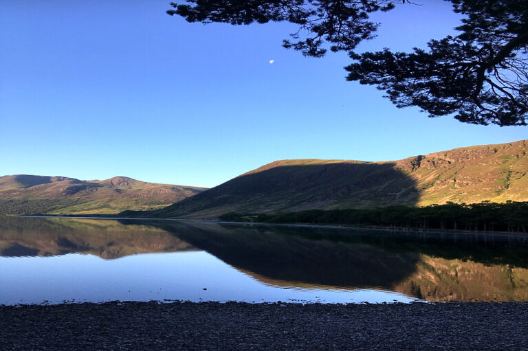 Calm lake reflecting mountains under clear blue sky