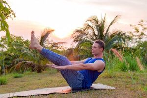Man practicing boat pose yoga at sunset outdoors