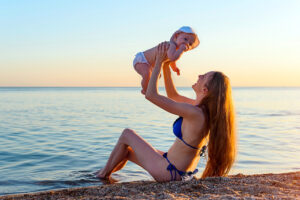 Mother lifting baby at sunset beach shoreline