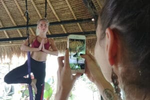 Woman practicing aerial yoga while photographed on smartphone