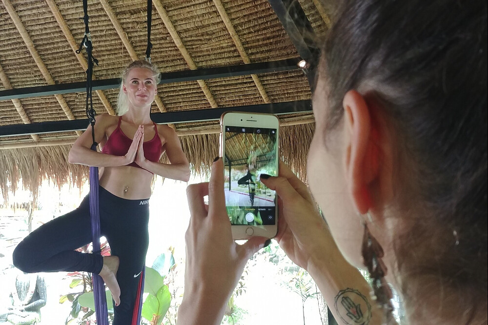 Woman practicing aerial yoga while photographed on smartphone