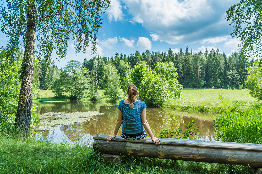 Woman sitting by pond in lush forest meadow