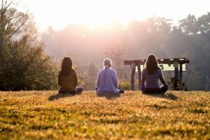 Three people meditating on grass at sunrise