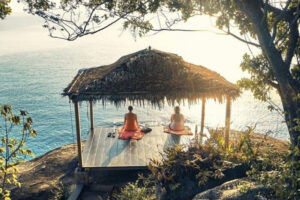 Two people meditating under hut by ocean