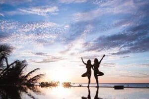 Two women practicing yoga at sunset by pool