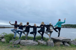 Seven friends balancing on rocks by shoreline