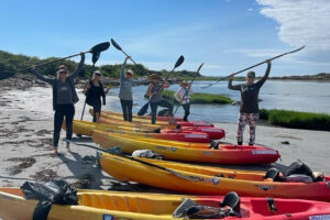 Group holding paddles beside colorful kayaks on beach