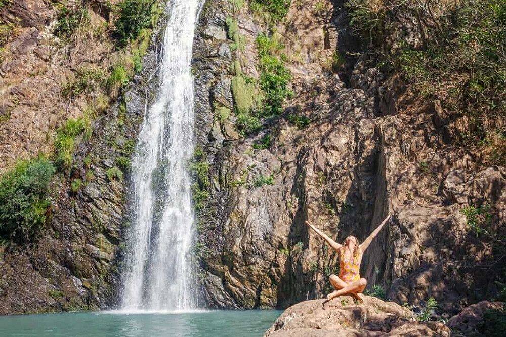 Woman meditating by waterfall on rocky cliff