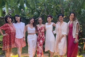 Seven women posing in lush tropical garden.