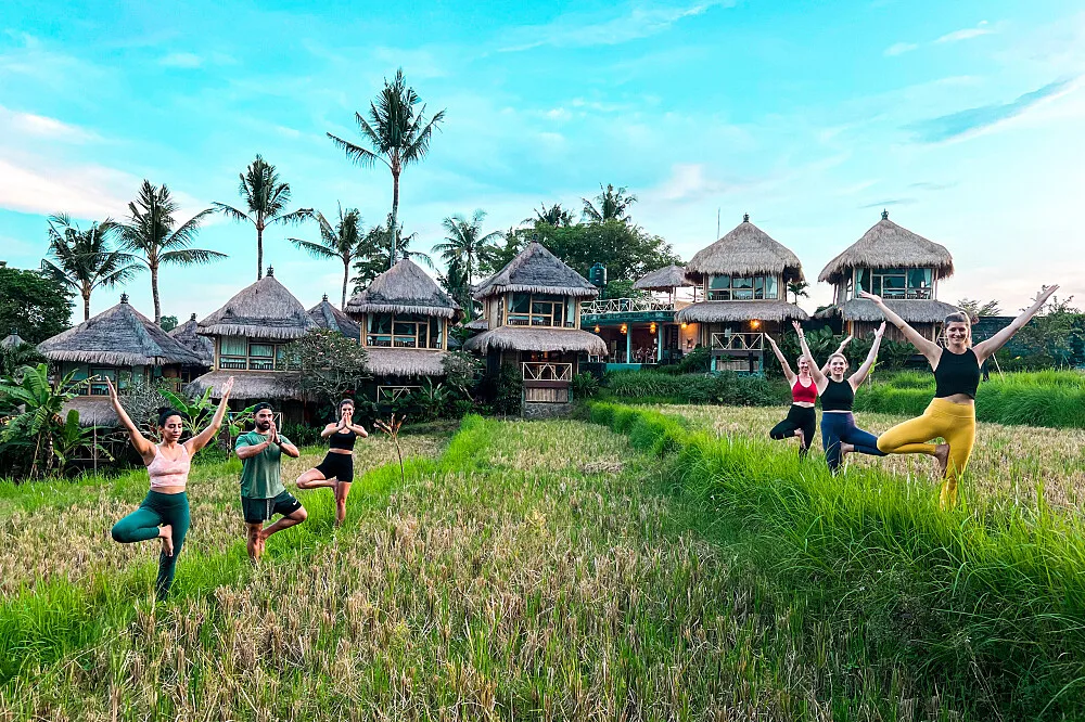 Group practicing yoga in tropical rice field resort