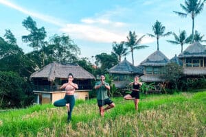 Three people practicing yoga in tropical resort field