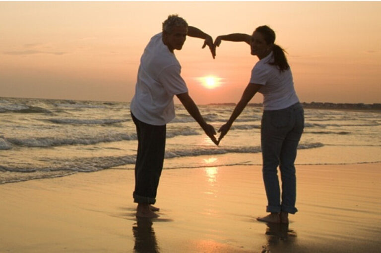 Couple forming heart shape at beach sunset