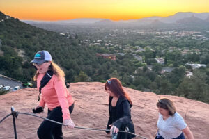 Three women hiking on rocky overlook at sunset