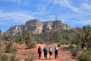 Four hikers on red desert trail toward cliffs
