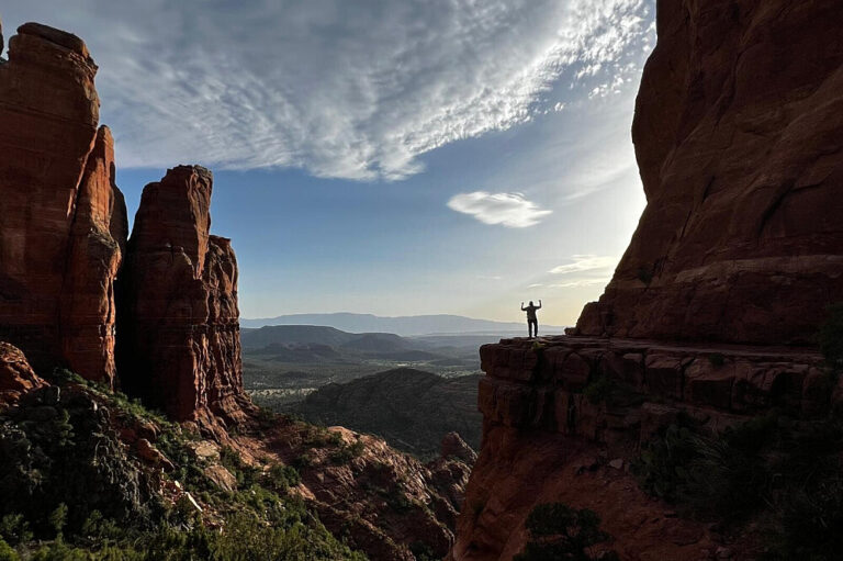 Hiker standing on cliff overlooking red rock canyon