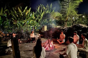 Group meditating around campfire in tropical garden at night