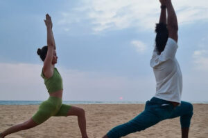 Two people doing yoga on beach at sunset