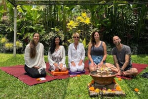 Five adults seated on mats in tropical garden