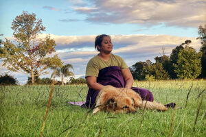 Woman meditating outdoors with dog on grass