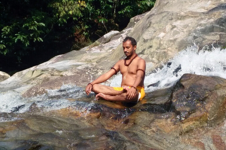 Man meditating on rocks beside waterfall