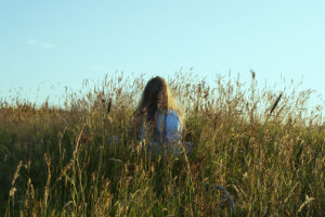 Person sitting in tall grass at sunset