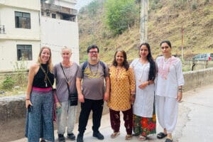 Six adults posing outdoors near hillside building