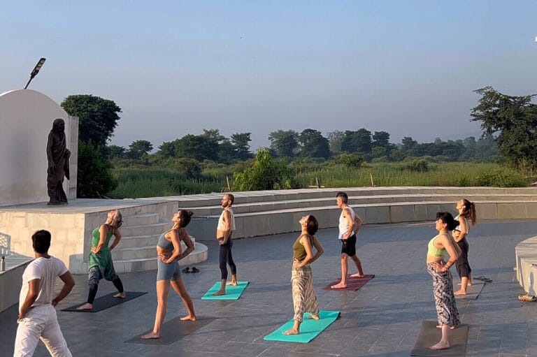 Group practicing yoga outdoors near statue
