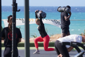 People doing sandbag lunges by the ocean